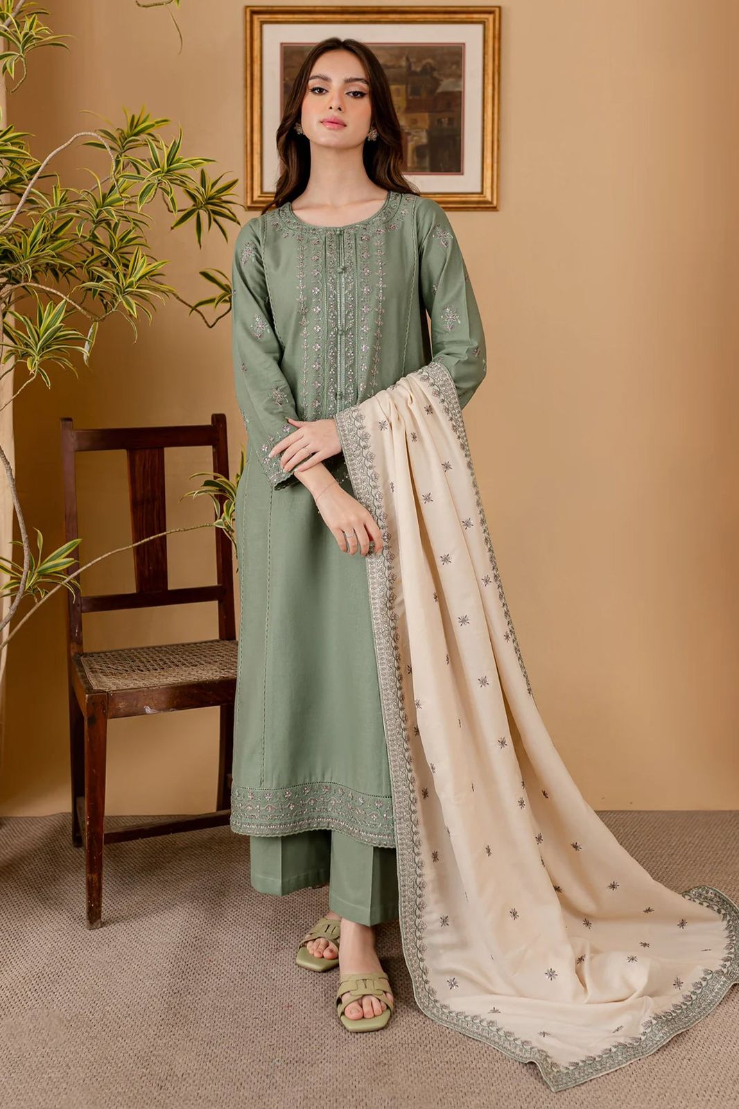 Woman in a green traditional outfit with a beige dupatta against a beige wall.